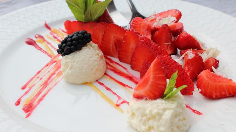 Ein schöner Teller mit frischen Erdbeeren, dekoriert mit schwarzen Johannisbeeren und Sahne. Die farbenfrohe Präsentation ist mit Saucen und Minzblättern verziert.