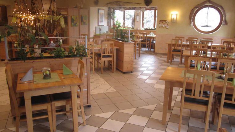 Ein einladendes Restaurant mit Holzstühlen und -tischen. Die Wände sind hell und mit Pflanzen dekoriert.