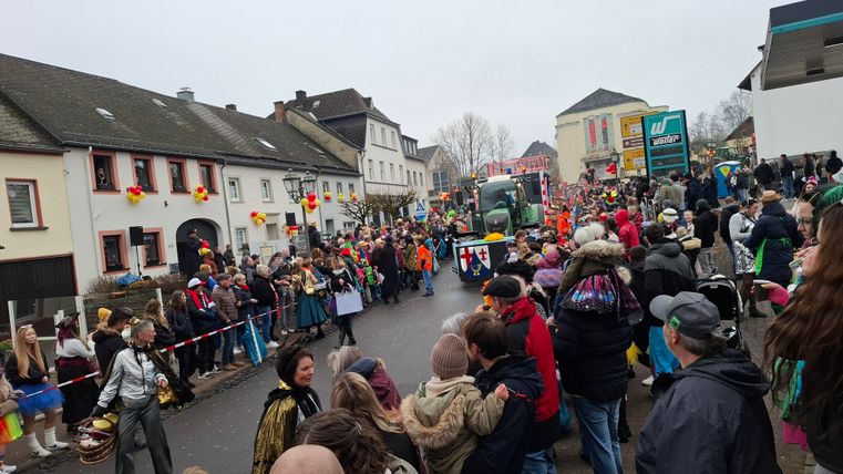 Ein bunter Umzug mit vielen Menschen auf der Straße. Es gibt festliche Kostüme und geschmückte Häuser.