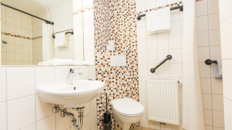 Ein modernes Badezimmer mit einer weißen Toilette, einem Waschbecken und einer Dusche. Die Wände sind teilweise mit dekorativen Fliesen gestaltet.