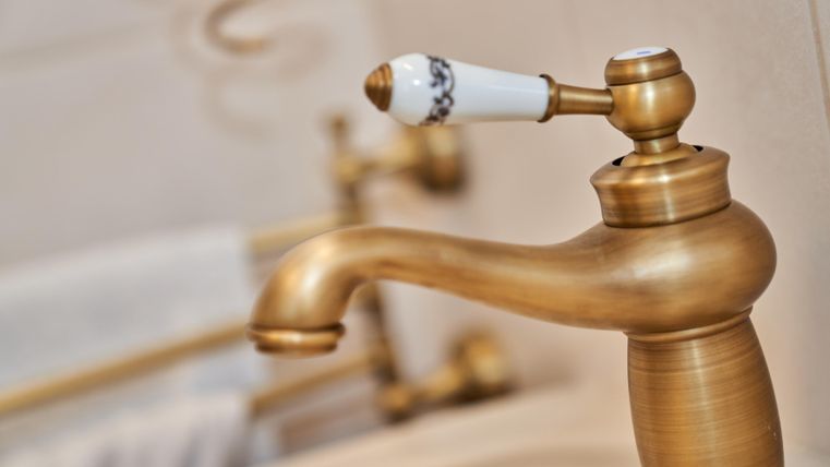 Eine elegante, goldfarbene Armatur mit einem weißen Griff. Im Hintergrund sind weiche Handtücher und weitere Badezimmerelemente zu erkennen.