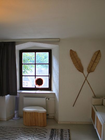 Ein gemütlicher Raum mit einem großen Fenster und einer modernen Einrichtung. An der Wand hängen dekorative Elemente aus Naturmaterialien.