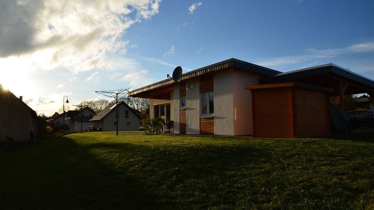 Ein modernes Haus mit einem Holzschuppen und einem schönen Garten. Die Sonne scheint am Himmel und schafft eine angenehme Atmosphäre.