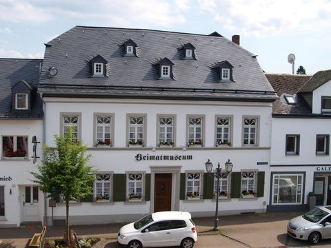 Ein historisches Gebäude mit der Aufschrift "Heimatmuseum". Es hat eine schöne Fassade mit ansprechenden Fenstern und ist von Bäumen umgeben.
