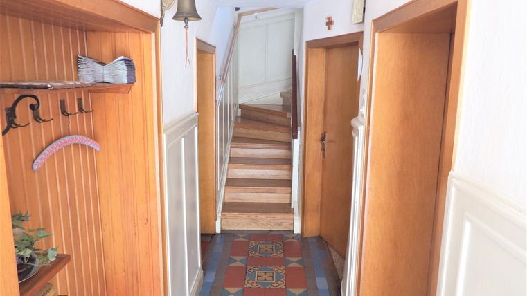 Ein heller Flur mit Holzverkleidung und einer klaren Treppe im Hintergrund. An den Wänden hängen einige Garderobenhaken und es gibt einen schönen Boden mit buntem Muster.