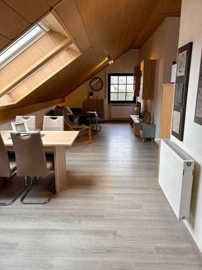 A modern living room with slanted walls and plenty of natural light. The space is furnished with a dining table, chairs, and a cozy seating area.
