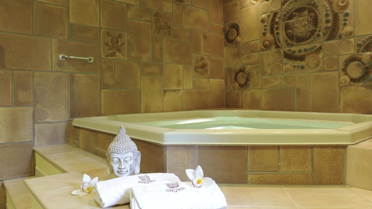 Ein elegantes Spa mit einem modernen Whirlpool und einer stilvollen Wandgestaltung. Frische Handtücher und eine Buddha-Statue ergänzen die entspannende Atmosphäre.