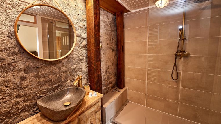 Ein modernes Badezimmer mit einem eleganten Waschtisch aus Stein und einer geräumigen Dusche. Die Kombination aus Holz und Stein verleiht dem Raum eine warme Atmosphäre.