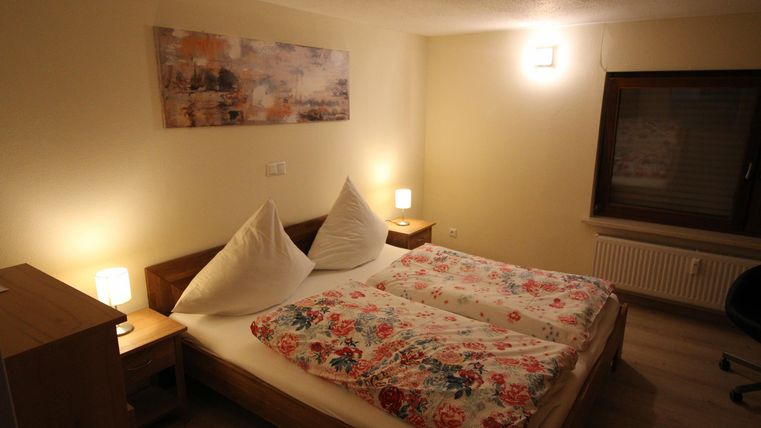 Ein gemütliches Schlafzimmer mit zwei Betten und bunten Bettdecken. Das Zimmer hat modernes Licht und ein großes Fenster.