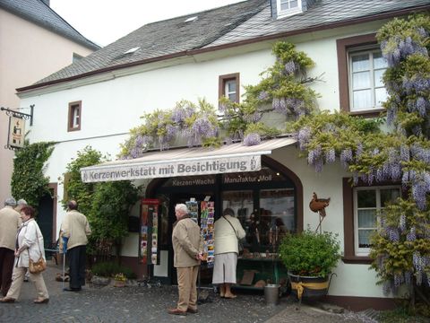Ein charmantes Gebäude mit blühendem Oleander und einem einladenden Eingang. Einige Besucher schauen sich die Angebote an.