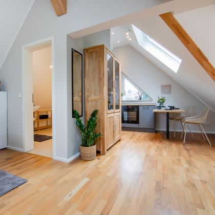 Eine gemütliche Dachgeschosswohnung mit Holzfußboden und einem großen Fenster. Der Raum ist hell und modern eingerichtet.