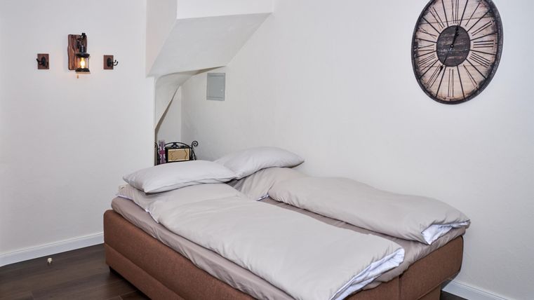 Ein gemütliches Schlafzimmer mit einem großen Bett und einer modernen Wanduhr. Die Wände sind hell gestrichen und der Boden ist aus Holz.