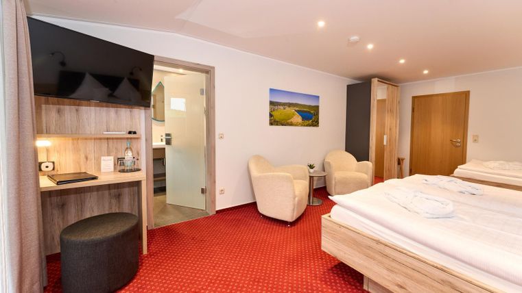 Ein modernes Hotelzimmer mit zwei Betten, einem Fernseher und einem kleinen Schreibtisch. Die Farben sind warm und einladend, mit einem komfortablen Sitzbereich.