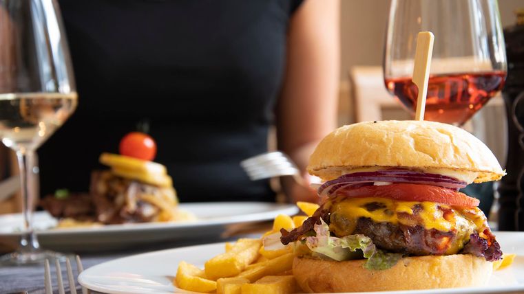 Ein köstlicher Hamburger mit Käse, frischem Gemüse und Pommes frites. Im Hintergrund sind weitere Speisen und Getränke zu sehen.