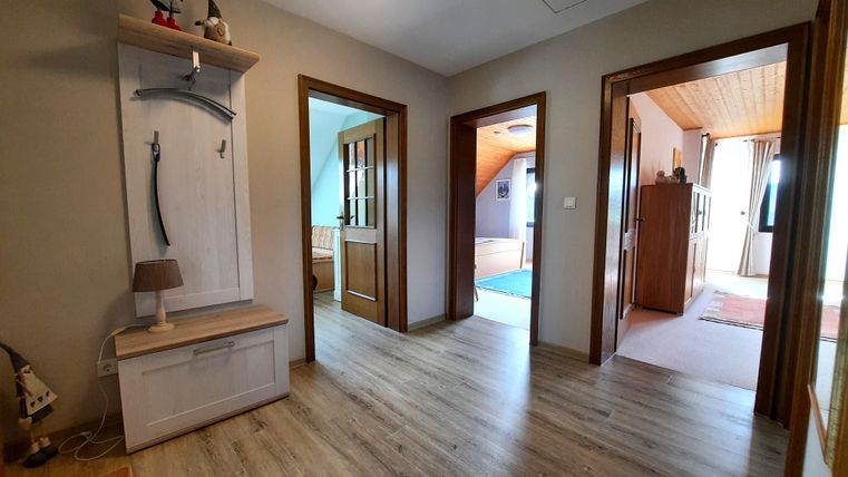 Ein heller Flur mit Holzfußboden und mehreren Türen, die zu anderen Räumen führen. Die Wände sind in neutralen Farben gehalten und es gibt einen kleinen Holzschrank.