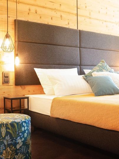 Ein modernes Schlafzimmer mit einem bequemen Bett und dekorativen Kissen. Die Holzwände und die sanfte Beleuchtung schaffen eine gemütliche Atmosphäre.