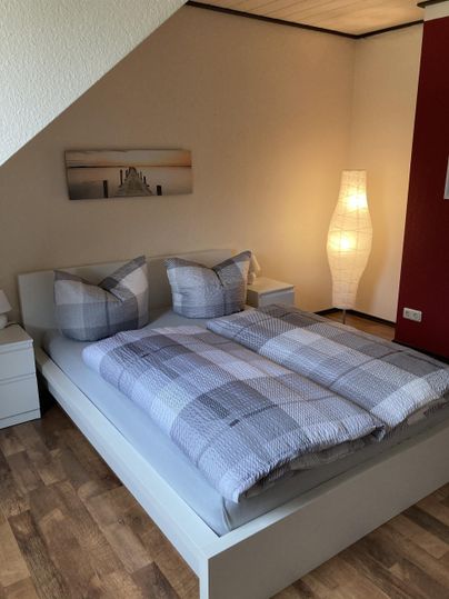 Ein gemütliches Schlafzimmer mit einem Doppelbett und modernen Kissen. Die warme Beleuchtung sorgt für eine einladende Atmosphäre.