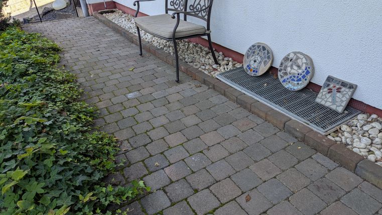 Eine gepflasterte Terrasse mit einer dekorativen Bank und bunten Tellern. Auf der linken Seite wächst grüne Pflanze.
