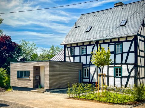 Ein modernes Haus mit einem Anbau und einem traditionellen Fachwerkstil. Umgeben von Bäumen und einem gemütlichen Weg.