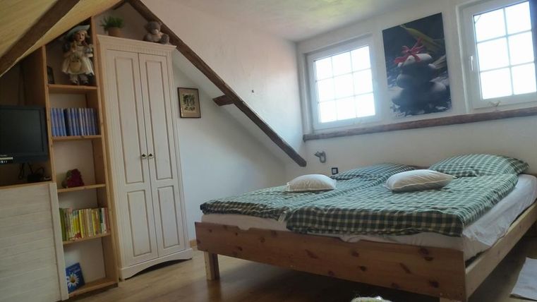 Ein helles Schlafzimmer mit einem großen Bett und zwei Kissen. An den Wänden hängen Bilder, und ein Schrank steht neben dem Fenster.