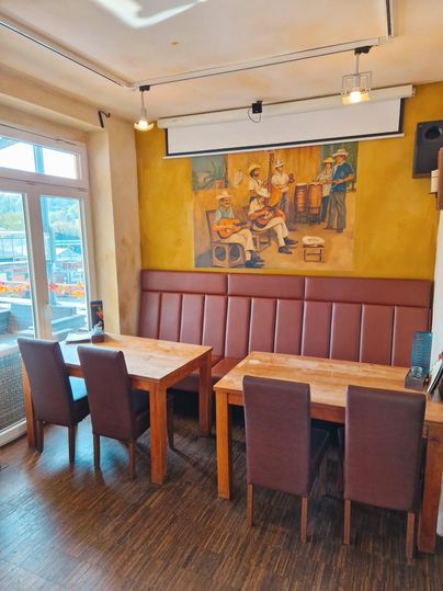 Ein gemütliches Restaurant mit Holztischen und Lederbänken. An der Wand hängt ein farbenfrohes Wandgemälde von musizierenden Menschen.