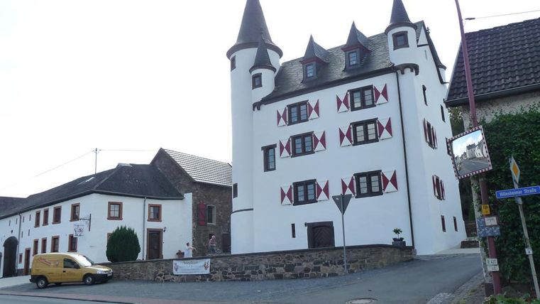 Ein charmantes, historisches Gebäude mit Türmen und bunten Fenstern. Es steht an einer straßenseitigen Ecke in einer kleinen Stadt.
