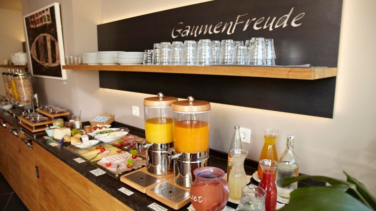 Eine Frühstücksbuffet mit frischen Säften, verschiedenen Speisen und Gläsern. Der Tisch ist ordentlich und einladend dekoriert.