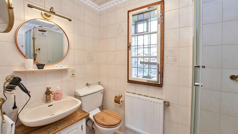 Ein modernes Badezimmer mit weißen Fliesen und einer Dusche. Der Waschtisch ist aus Holz und hat einen runden Spiegel.