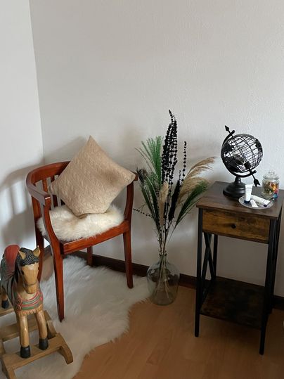 Ein gemütlicher Wohnbereich mit einem Holzstuhl, einem Kissen und einer kleinen Globus-Dekoration. Neben dem Stuhl steht eine Vase mit Pflanzen und ein kleiner Tisch.