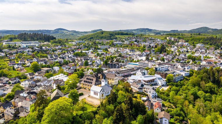 Eine malerische Ansicht einer Stadt umgeben von grünen Hügeln und Bäumen. Die Gebäude sind gut verteilt und die Landschaft ist einladend.