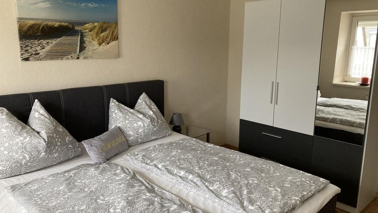 Ein helles Schlafzimmer mit zwei Einzelbetten und modernen Kissen. Im Hintergrund hängt ein Bild von einem Strand und ein großer Schrank steht an der Wand.