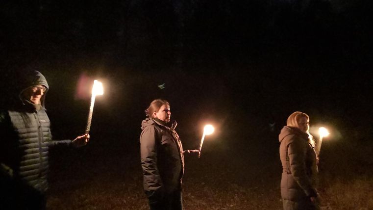 Een groep mensen staat in het donker en houdt fakkels vast. De sfeer is mystiek en geheimzinnig.