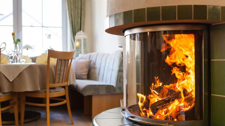 Ein moderner Kamin mit flammendem Feuer in einem gemütlichen Raum. Im Hintergrund sind ein Tisch und Stühle sichtbar, die eine einladende Atmosphäre schaffen.