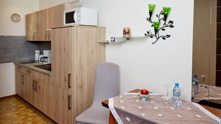 Eine moderne Kücheneinheit mit Holzschränken und einer Mikrowelle. Ein kleiner Essbereich mit einem Tisch und einem Stuhl ist ebenfalls zu sehen.