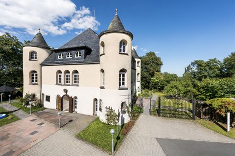Ein schönes, modernes Schloss mit einem großen Garten. Der Himmel ist klar und blau, umgeben von Bäumen.