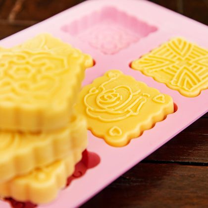 Eine pinke Silikonform mit gelben, geometrisch geformten Backwaren. Die Kekse haben verschiedene Muster und sind auf einem Holztisch angeordnet.