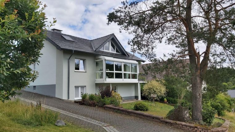 Ein modernes Haus mit großen Fenstern und einem gepflegten Garten. Die Umgebung ist grün und einladend, ideal für eine ruhige Wohnatmosphäre.
