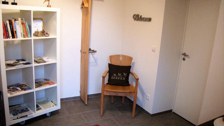 Ein einladender Eingangsbereich mit einem Bücherregal und einem Stuhl. Die Wände sind hell und modern gestaltet, mit einem roten Teppich und einem Willkommensschild.