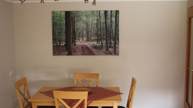 Ein Essbereich mit einem Holztisch und Stühlen. An der Wand hängt ein großes Bild eines waldbedeckten Pfades.