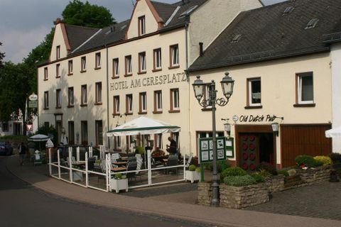 Ein Gebäude mit dem Namen "Hotel am Ceresplatz" und einem Restaurant namens "Old Dutch Pub". Im Vordergrund sind Tische im Freien und eine ruhige Straße zu sehen.
