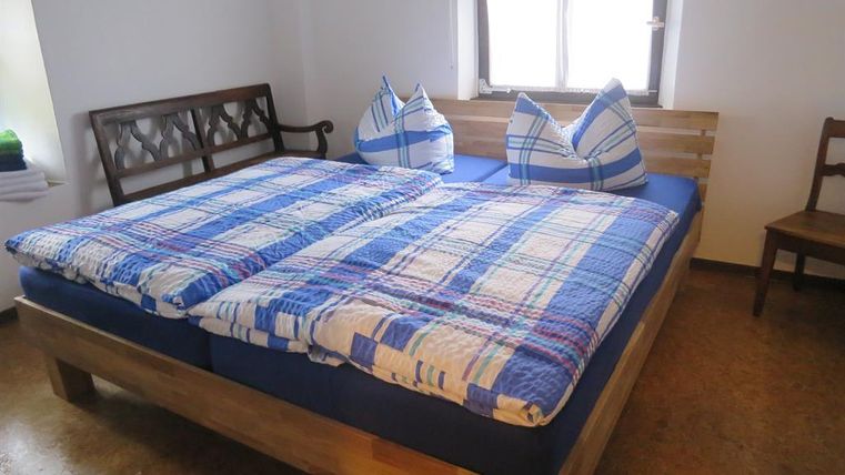 Ein gemütliches Schlafzimmer mit einem großen Bett und blauen karierten Bettdecken. Zwei Kissen in Form von Hügeln stehen auf dem Bett, und ein Fenster sorgt für natürliches Licht.