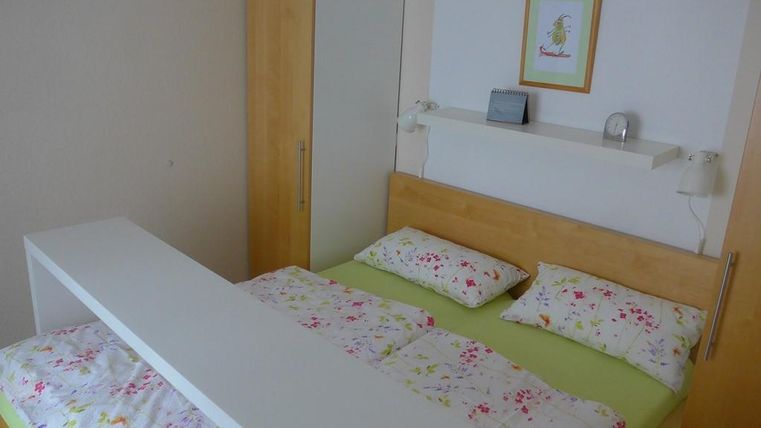 Ein einfaches Schlafzimmer mit einem Doppelbett und bunten Bettwäsche. Im Hintergrund befindet sich ein Kleiderschrank und ein Wandregal.