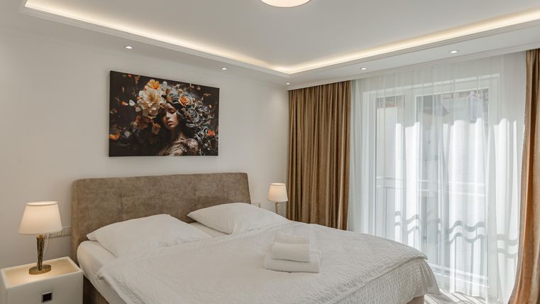 Ein modernes Schlafzimmer mit einem großen Bett und einer stilvollen Wandkunst. Große Fenster lassen viel Licht herein und schaffen eine gemütliche Atmosphäre.