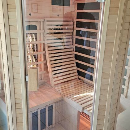 Eine moderne Sauna mit einem Holzinterieur und einem bequemen Liegebereich. Die Sauna hat eine klare Glasfront und sanfte Beleuchtung.
