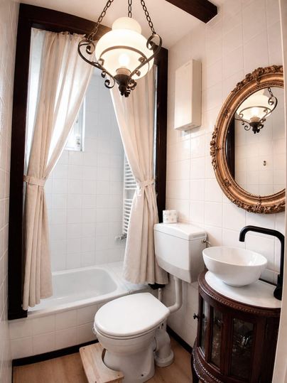 Ein kleines Badezimmer mit einer Badewanne, einem Waschbecken und einer Toilette. Elegante Elemente wie ein Spiegel und eine Lampe verleihen dem Raum Charme.