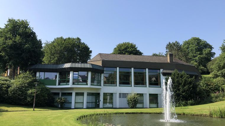 Een modern huis met grote ramen en een onderhouden tuin. Op de voorgrond is een vijver met een waterval.