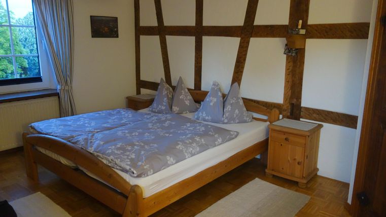 Ein gemütliches Schlafzimmer mit einem großen Bett und Holzmöbeln. Die Wände sind im rustikalen Stil mit sichtbaren Balken gestaltet.