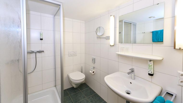 Ein modernes Badezimmer mit Dusche und Waschbecken. Die Wände sind gefliest und es gibt handtücher in einem frischen Blau.