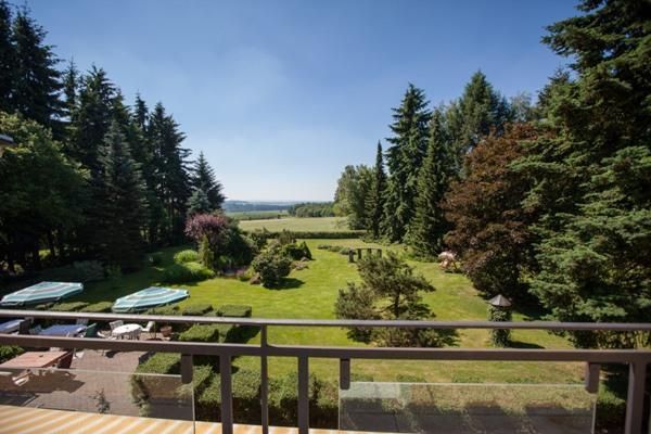Ein schöner Garten mit gepflegten Rasenflächen und hohen Bäumen. Im Hintergrund ist eine weite Landschaft zu sehen unter klarem Himmel.