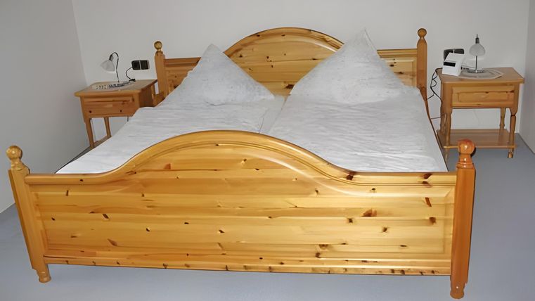 Ein einfaches Schlafzimmer mit einem Holzbett und zwei Nachttischen. Die Bettwäsche ist weiß und die Wände sind hell.